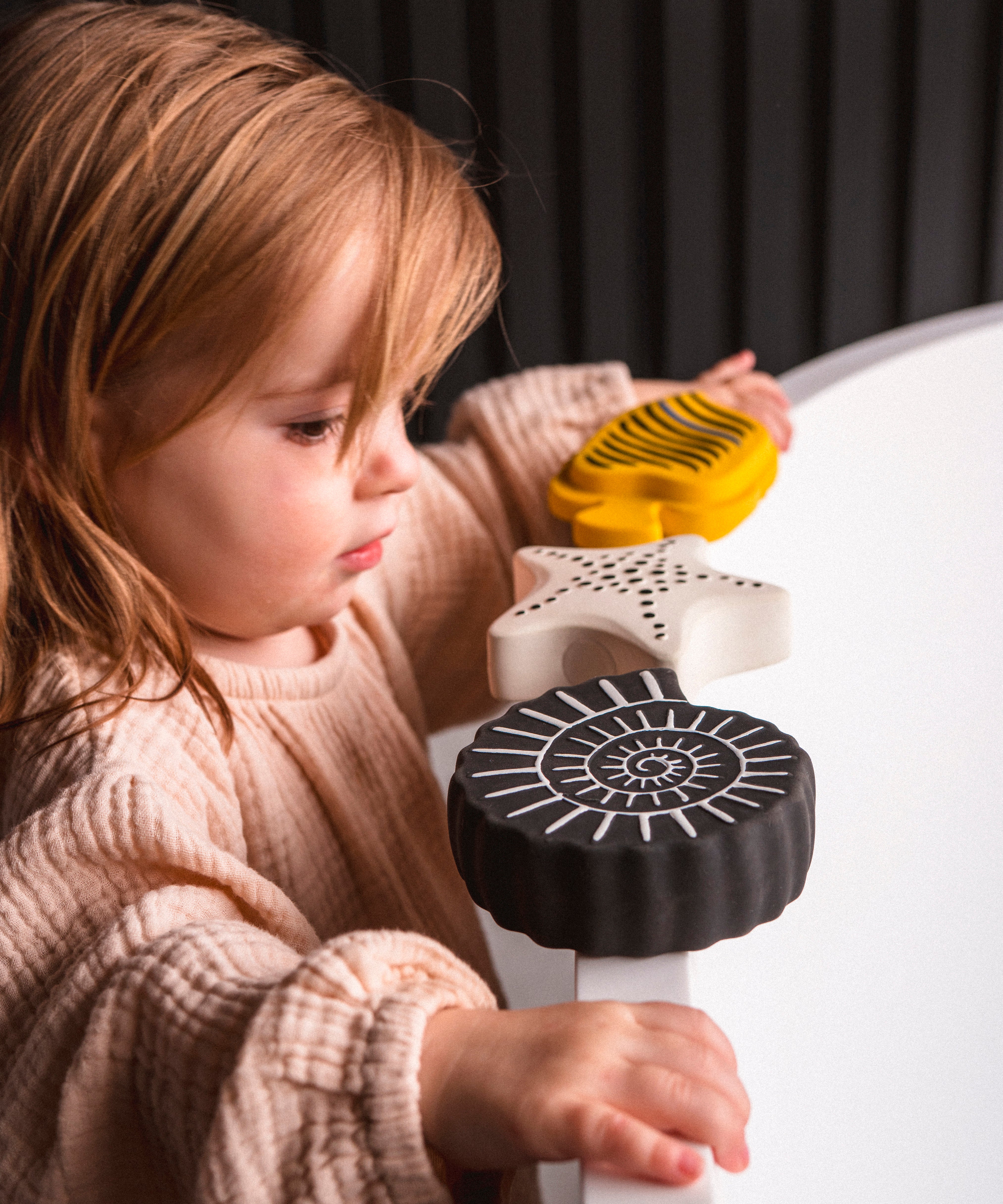 A toddler standing next to a bath with the Etta loves sensory bath toys on the rim