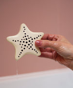 A adult hand holding the starfish bath toy from the Etta Loves sensory bath toy set