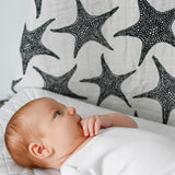A baby lying down and looking up at the XL Starfish muslin cloth 