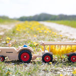 Fagus handmade wooden tractor and hay cart toy on a grass field carrying some dandelions