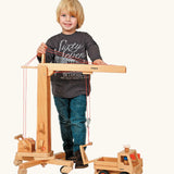 Child standing next to the Fagus handmade wooden crane toy and unimog truck.