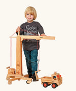 Child standing next to the Fagus handmade wooden crane toy and unimog truck.