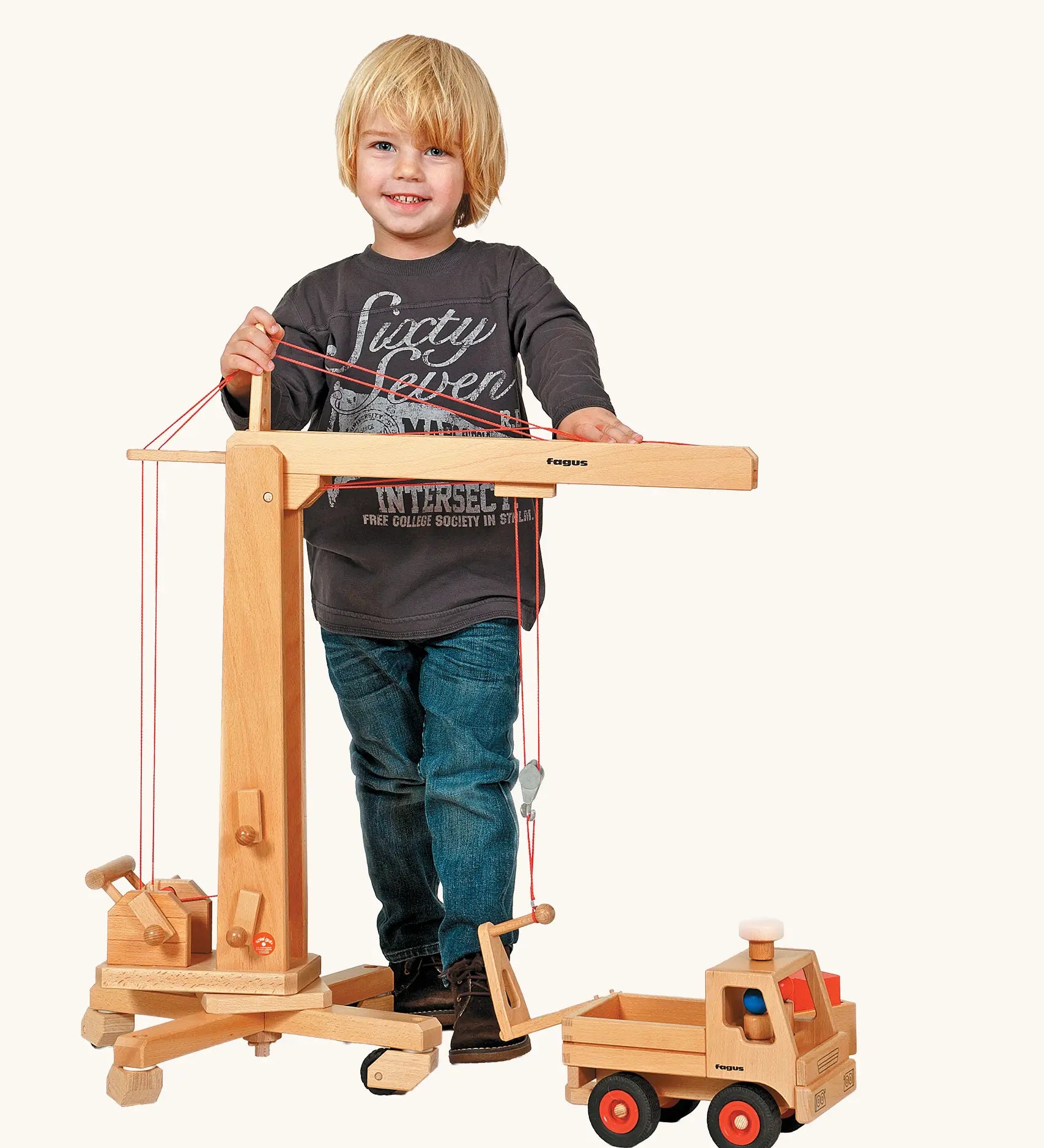 Child standing next to the Fagus handmade wooden crane toy and unimog truck.
