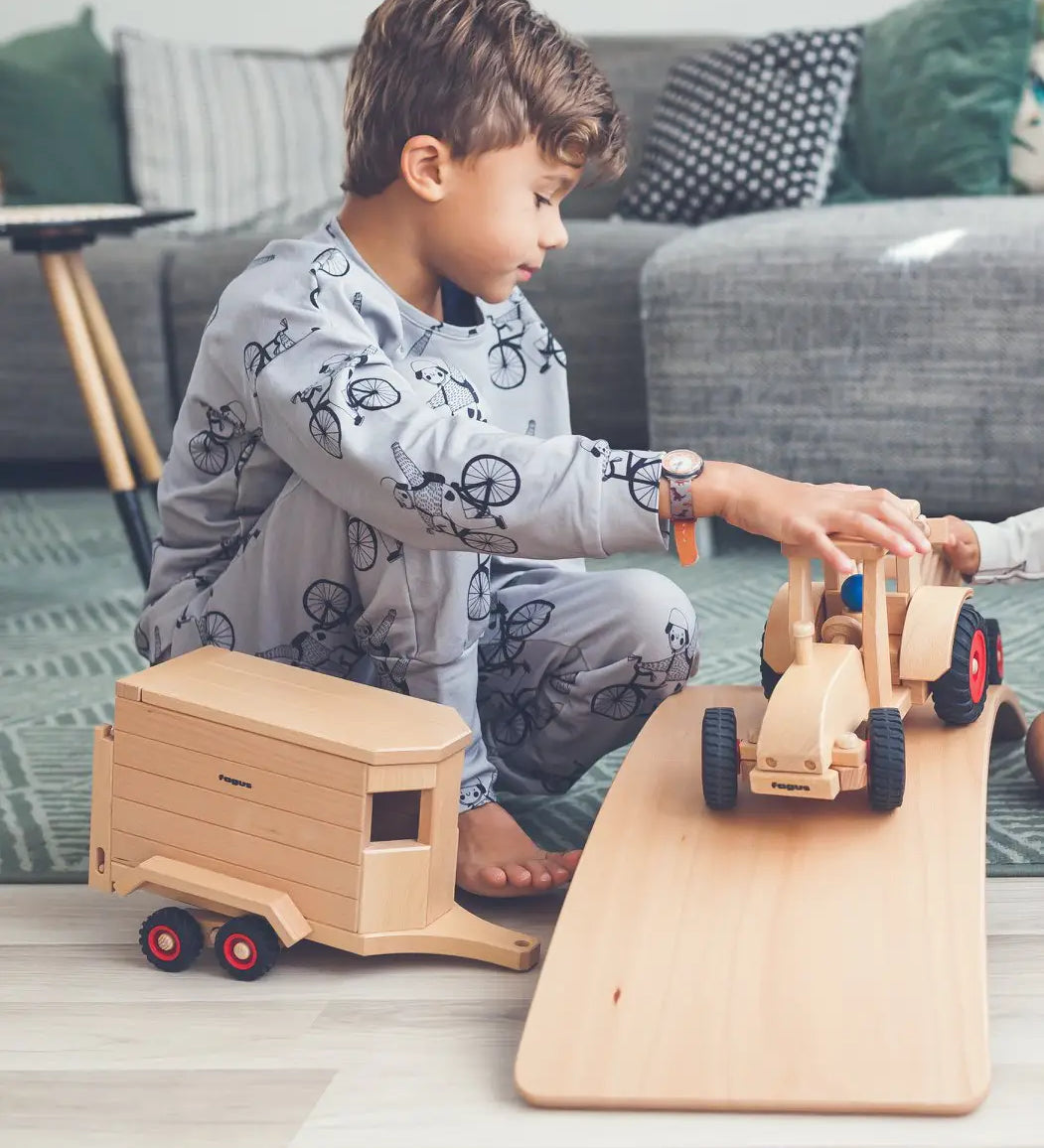 Child playing with the Fagus modern tractor and wooden horse box toy on a wooden balance board.