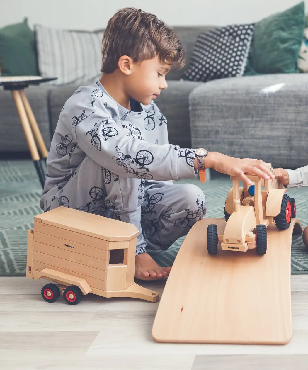 Child playing with the Fagus modern tractor and wooden horse box toy on a wooden balance board.