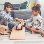 Two children playing with the Fagus modern tractor and wooden horse box toy on a wooden balance board in a grey living room