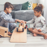 Two children playing with the Fagus modern tractor and wooden horse box toy on a wooden balance board in a grey living room