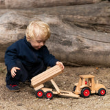 Child playing with the Fagus wooden trailer toy holding the trailer bed up next to a tractor ready to hitch in on.