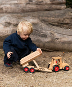 Child playing with the Fagus wooden trailer toy holding the trailer bed up next to a tractor ready to hitch in on.