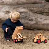 Child playing with the Fagus wooden trailer toy holding the trailer bed up next to a tractor.