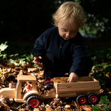 Child playing with the Fagus wooden trailer hitched onto a tractor, filling the trailer with leaves and conkers.