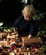 Child playing with the Fagus wooden trailer hitched onto a tractor, filling the trailer with leaves and conkers.