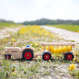 Fagus handmade wooden hay wagon toy attachment hitches onto the tractor with the trailer filled with yellow dandelions.