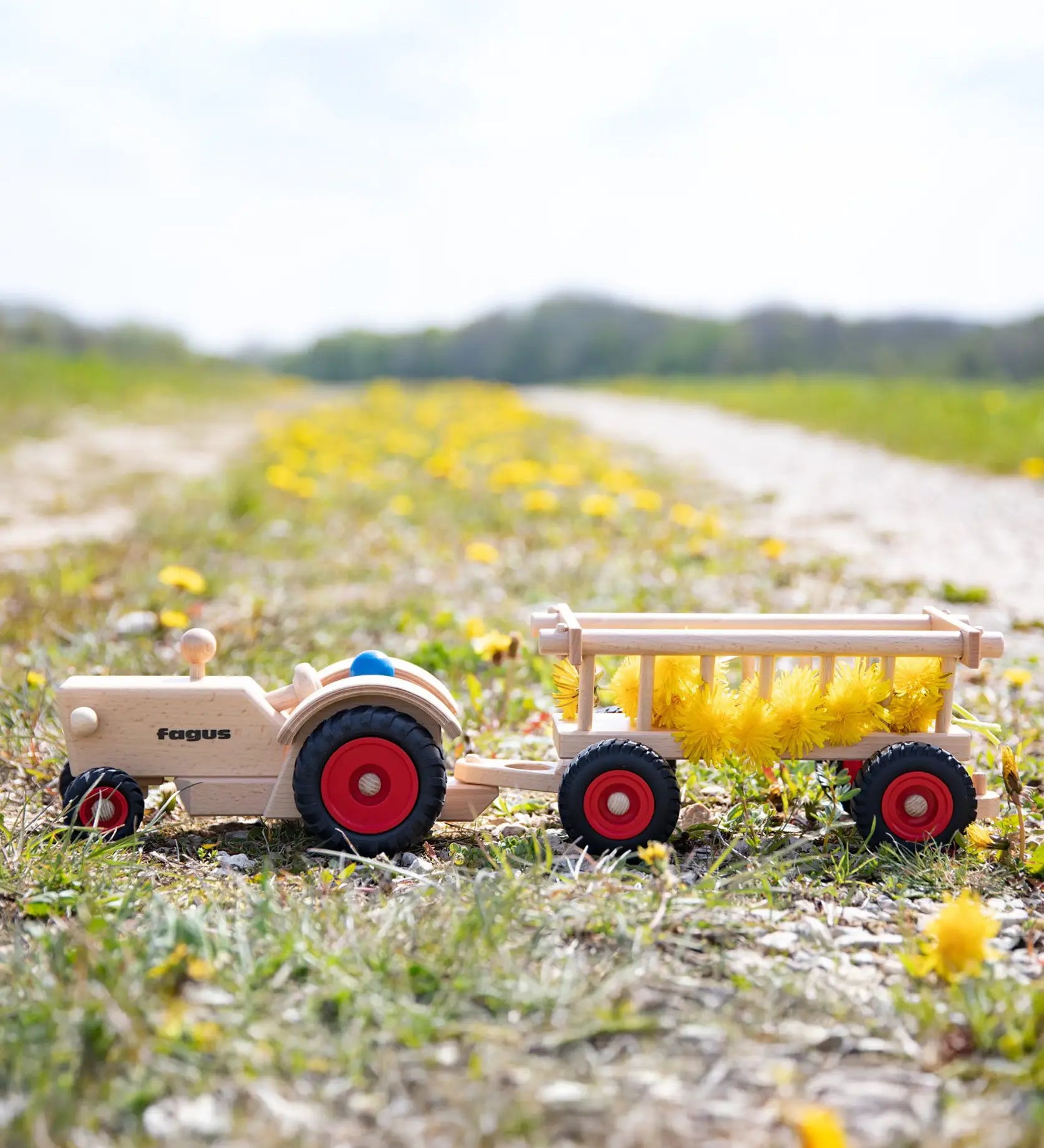Fagus handmade wooden hay wagon toy attachment hitches onto the tractor with the trailer filled with yellow dandelions.