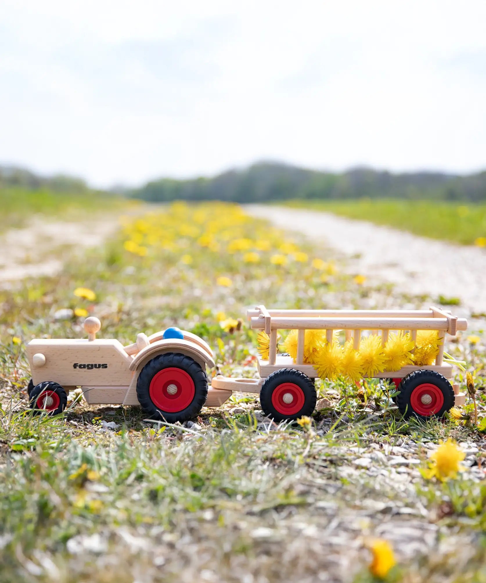 Fagus handmade wooden hay wagon toy attachment hitches onto the tractor with the trailer filled with yellow dandelions.