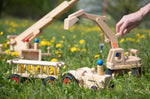Fagus handmade wooden hay wagon toy attachment hitches onto the tractor with the trailer filled with yellow dandelions. Other Fagus vehicles can be seen in the background.