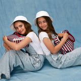 Children sitting, one is holding a Fluf GOTS organic cotton square lunch bag in a awning stripe chili pepper design, the other has a matching zipper lunch bag.