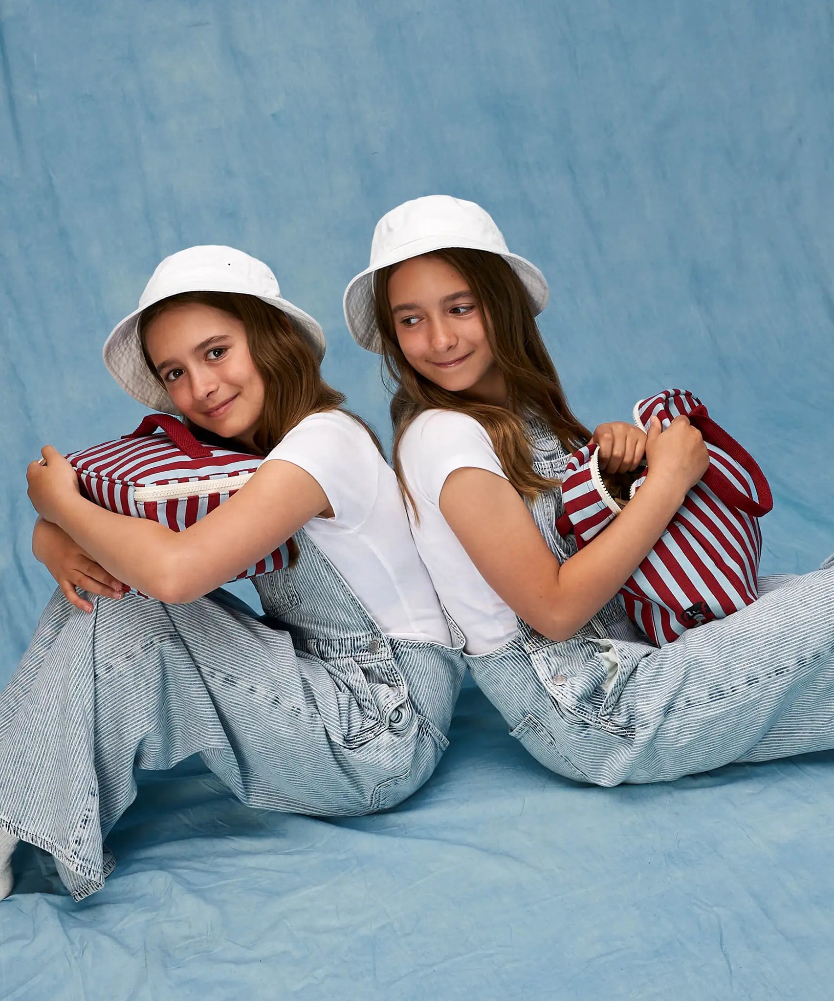 Children sitting, one is holding a Fluf GOTS organic cotton square lunch bag in a awning stripe chili pepper design, the other has a matching zipper lunch bag.
