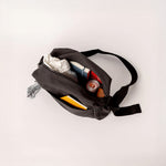A top view of the Fluf organic cotton crossbody bag with sectioned pockets, showing items that fit inside 