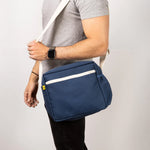 A side view of a man's torso, who's carrying the Fluf organic cotton everyday lunch crossbody bag in navy blue with a white strap.