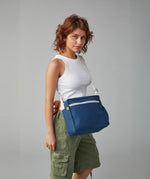 A woman wearing the organic cotton Fluf crossbody bag in navy blue with a white adjustable strap. 