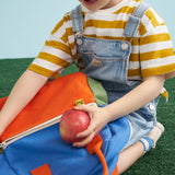 A close up of a child placing an apple in the front zipped pocket on a Fluf kids junior organic cotton backpack. 
