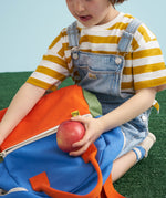 A close up of a child placing an apple in the front zipped pocket on a Fluf kids junior organic cotton backpack. 