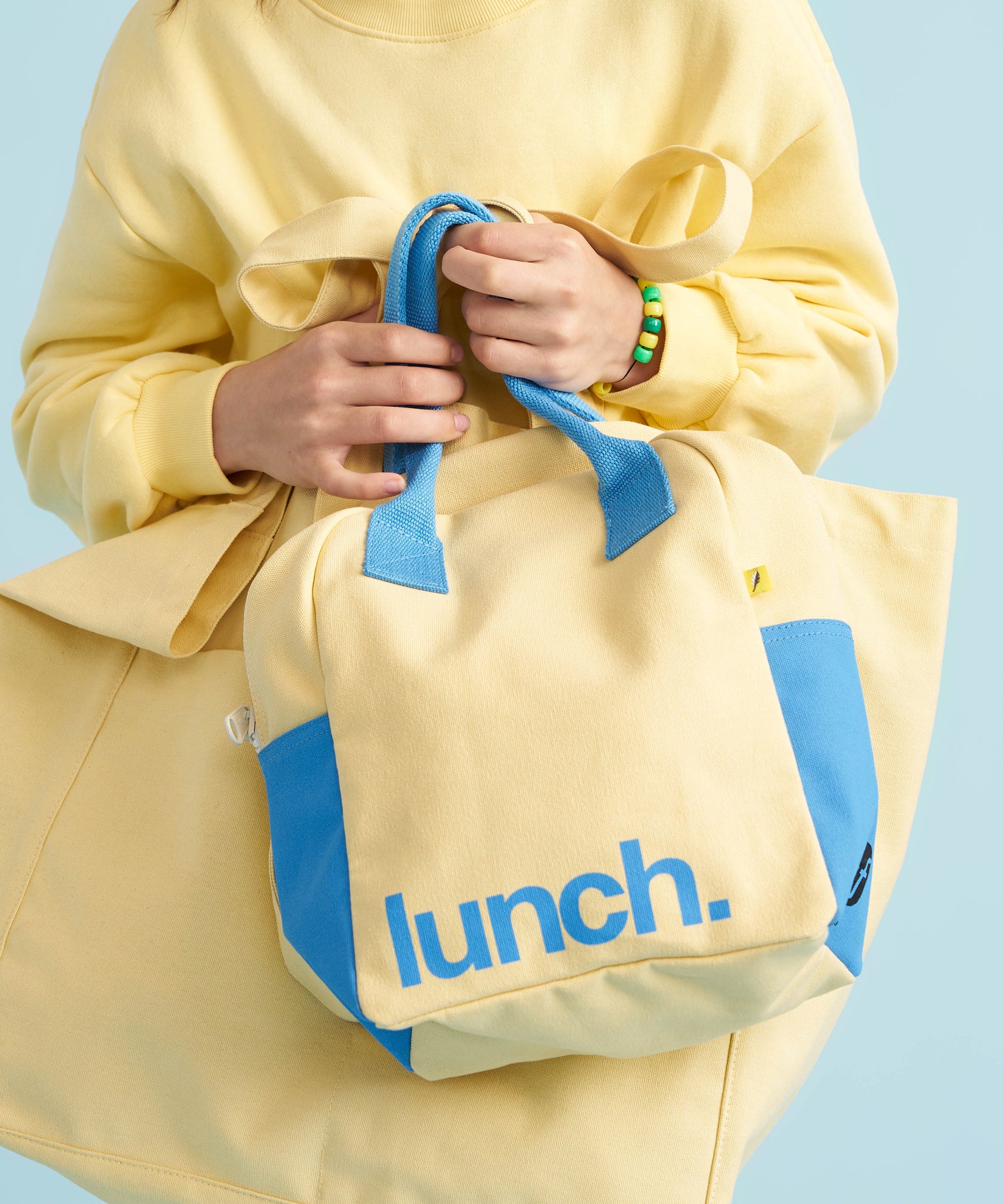 A close up of a person holding the Fluf organic cotton zippered lunch bag in a light butter yellow colour. 