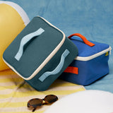 Fluf GOTS organic cotton square lunch bag in a cypress with a white zip detail. Features a light blue carry handle on the top and side. A bag in another colourway has been placed underneath.