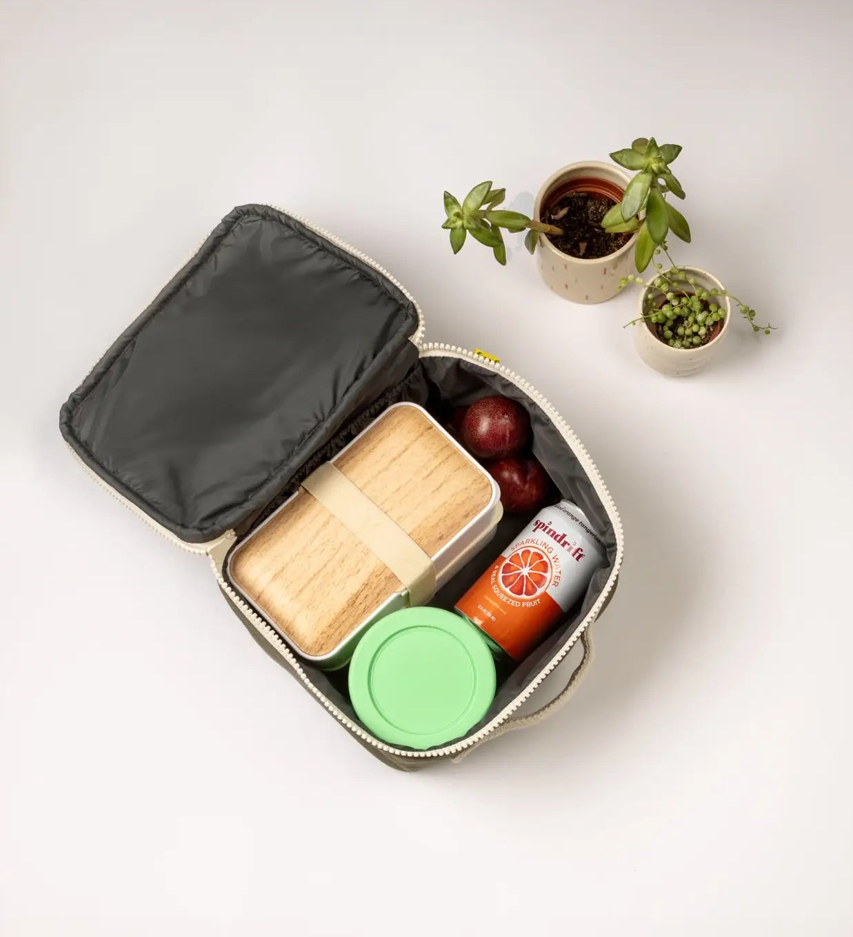 An open Fluf square lunch bag showing food and drink items inside. Lunch bag features a a rinseable, food-safe lining