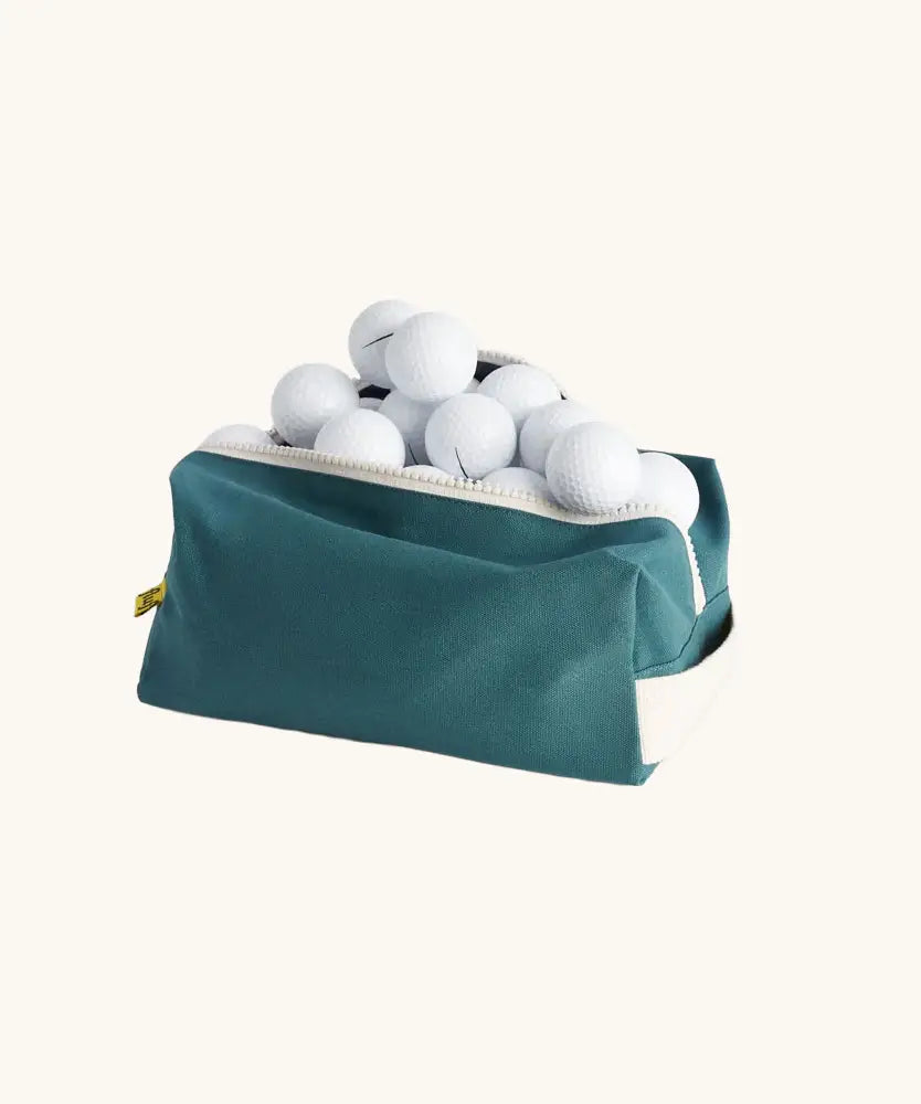 Fluf Traveller Bag in cypress green filled with golf balls, shown with zip open.
