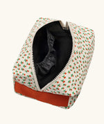 Overhead view of the Fluf Traveller Bag in tiny rose print, a compact organic cotton washbag with orange red carry handle and zip. Zip shown open.