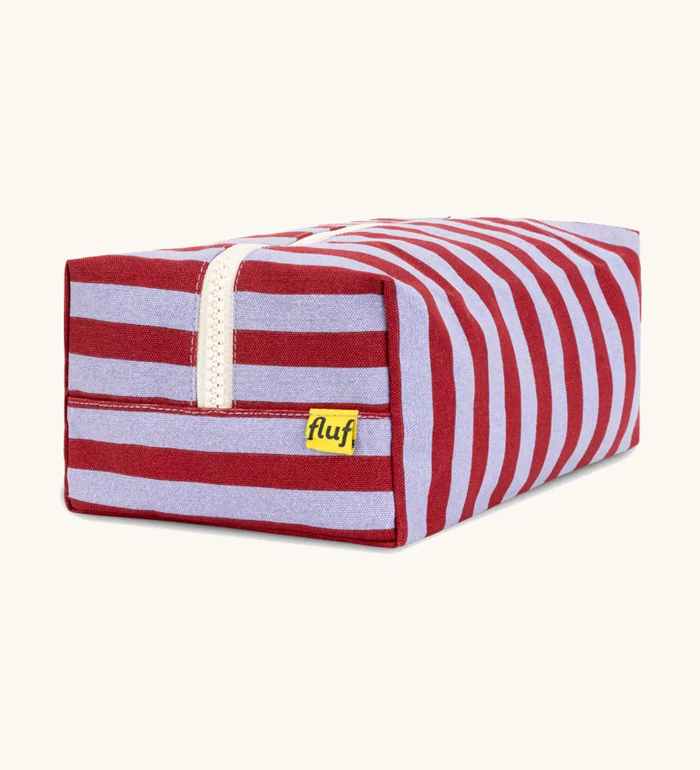 Side view of the Fluf Traveller Bag in Awning Stripe Chili Pepper, showing the striped organic cotton outer, cream zip, and Fluf label.