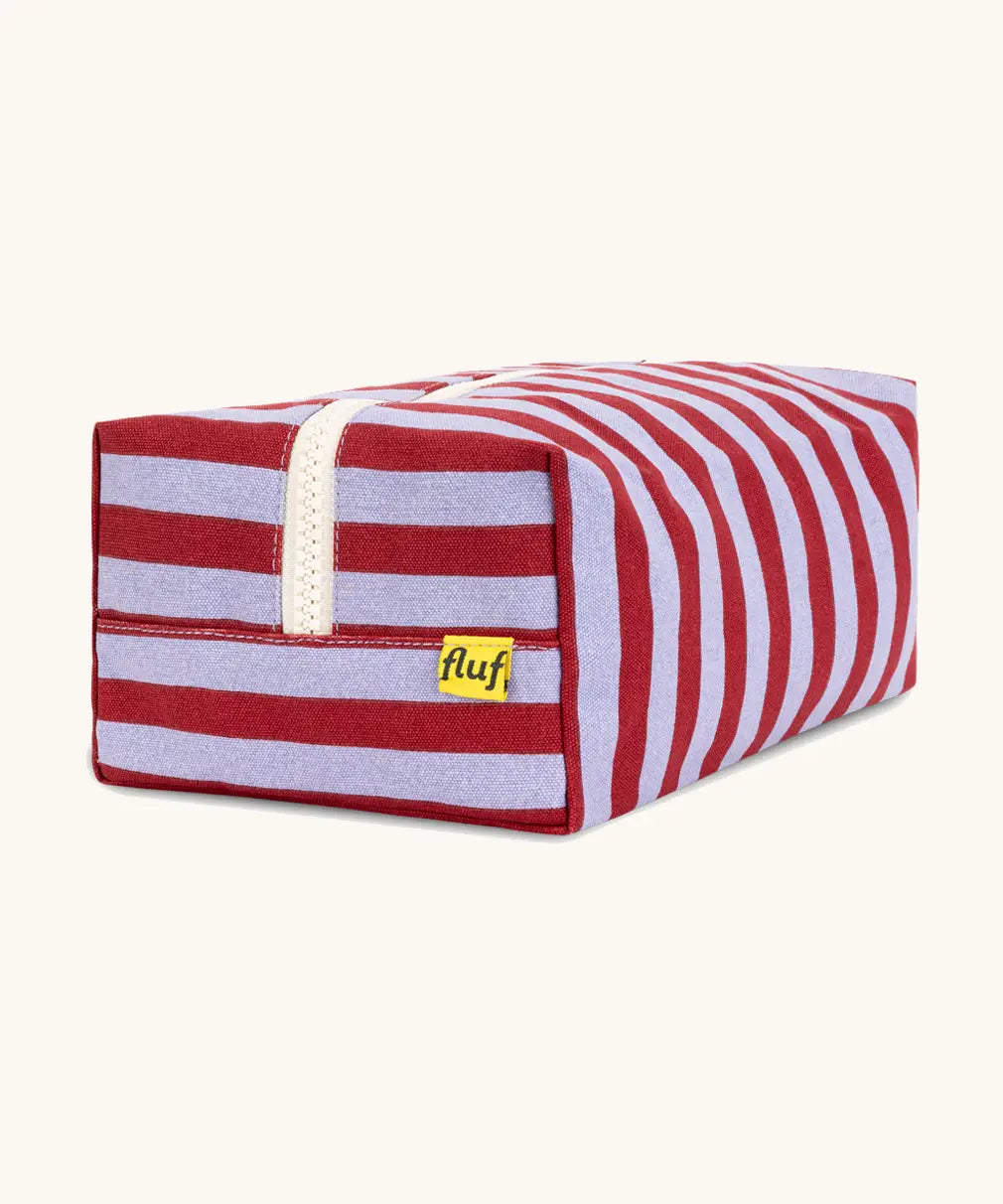 Side view of the Fluf Traveller Bag in Awning Stripe Chili Pepper, showing the striped organic cotton outer, cream zip, and Fluf label.