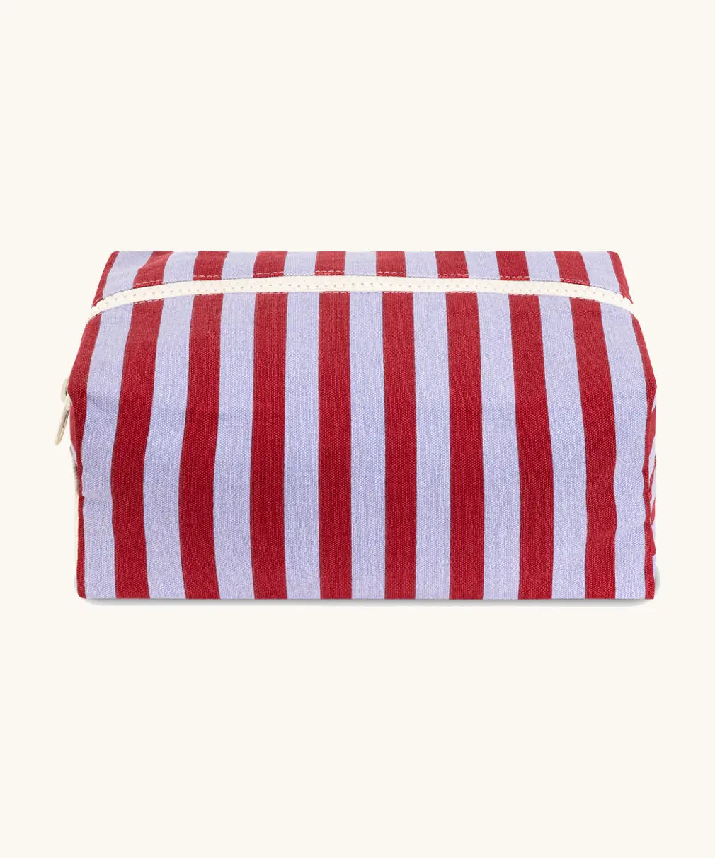 Fluf Traveller Bag in Awning Stripe Chili Pepper, the organic cotton washbag is closed from the front with cream zip and striped fabric.