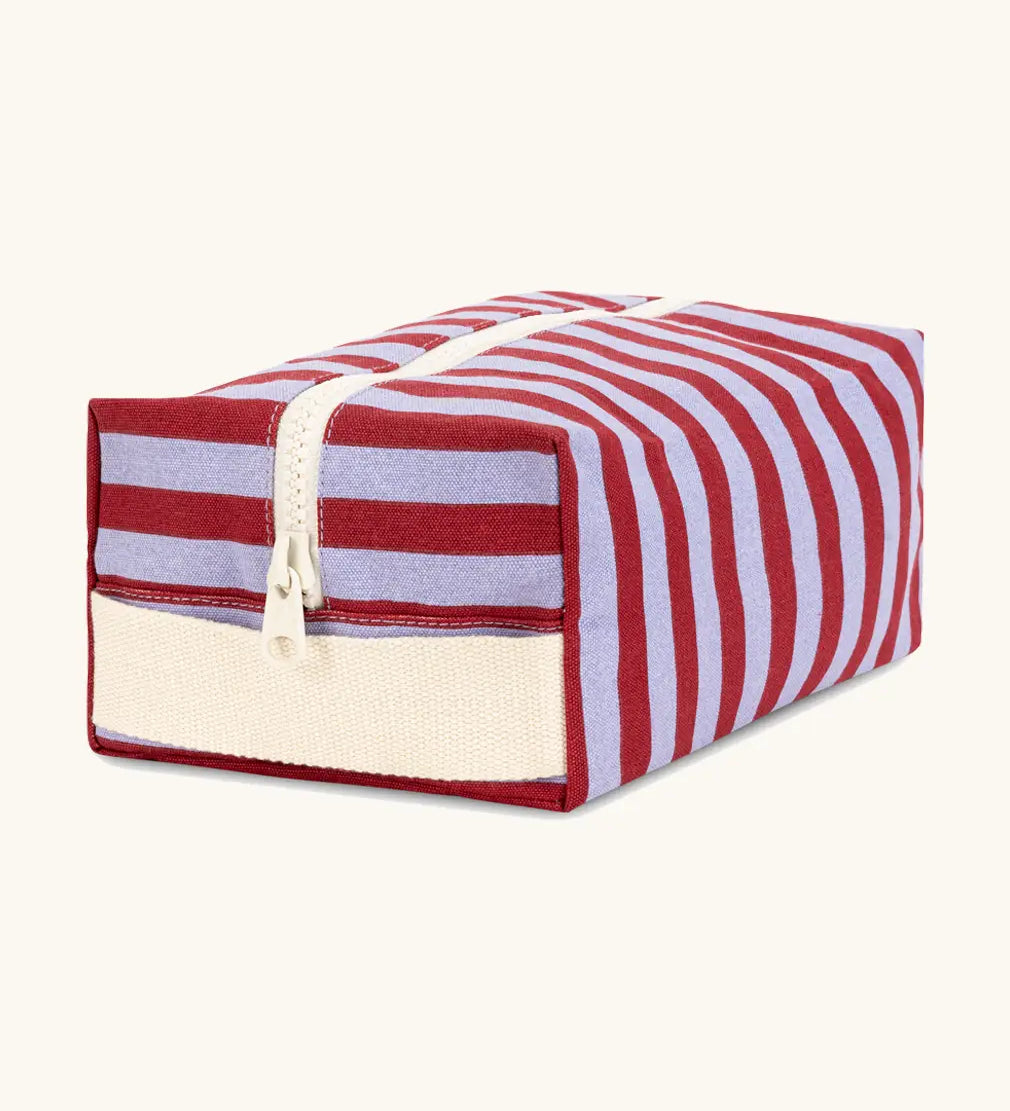 Angled front view of the Fluf Traveller Bag in Awning Stripe Chili Pepper, a compact organic cotton washbag with cream carry handle and zip.