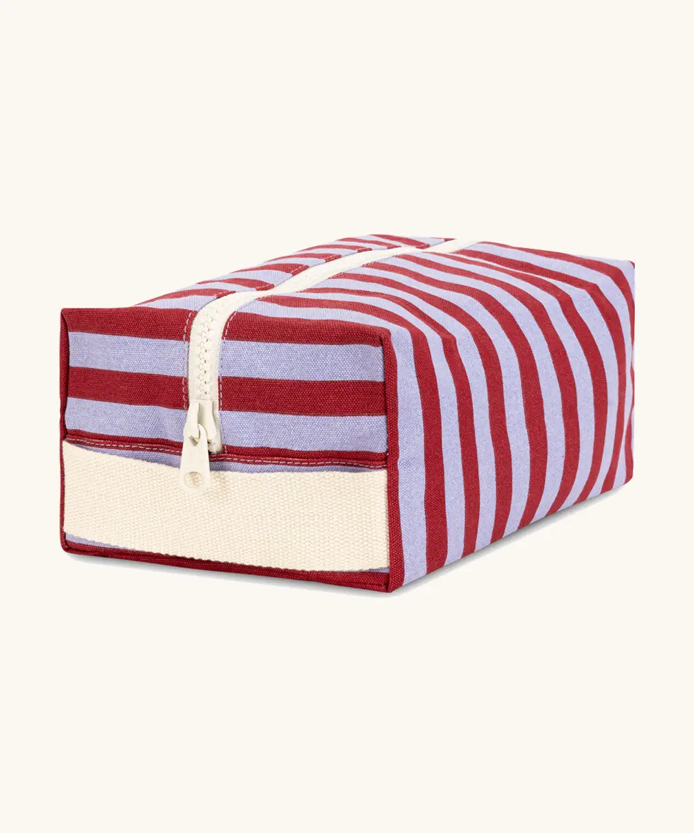 Angled front view of the Fluf Traveller Bag in Awning Stripe Chili Pepper, a compact organic cotton washbag with cream carry handle and zip.