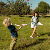 Children playing with the Flup throwing game outdoors. Each child is holding one of the fabric slings and the throwing bag is up in the air. 