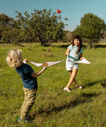 Children playing with the Flup throwing game outdoors. Each child is holding one of the fabric slings and the throwing bag is up in the air. 