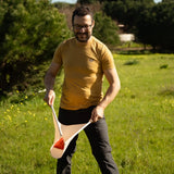 An adult playing the Flup throwing game outdoors, holding one of the fabric slings with the soft throwing bag balanced on it. 