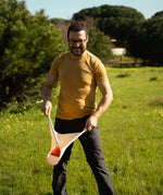 An adult playing the Flup throwing game outdoors, holding one of the fabric slings with the soft throwing bag balanced on it. 