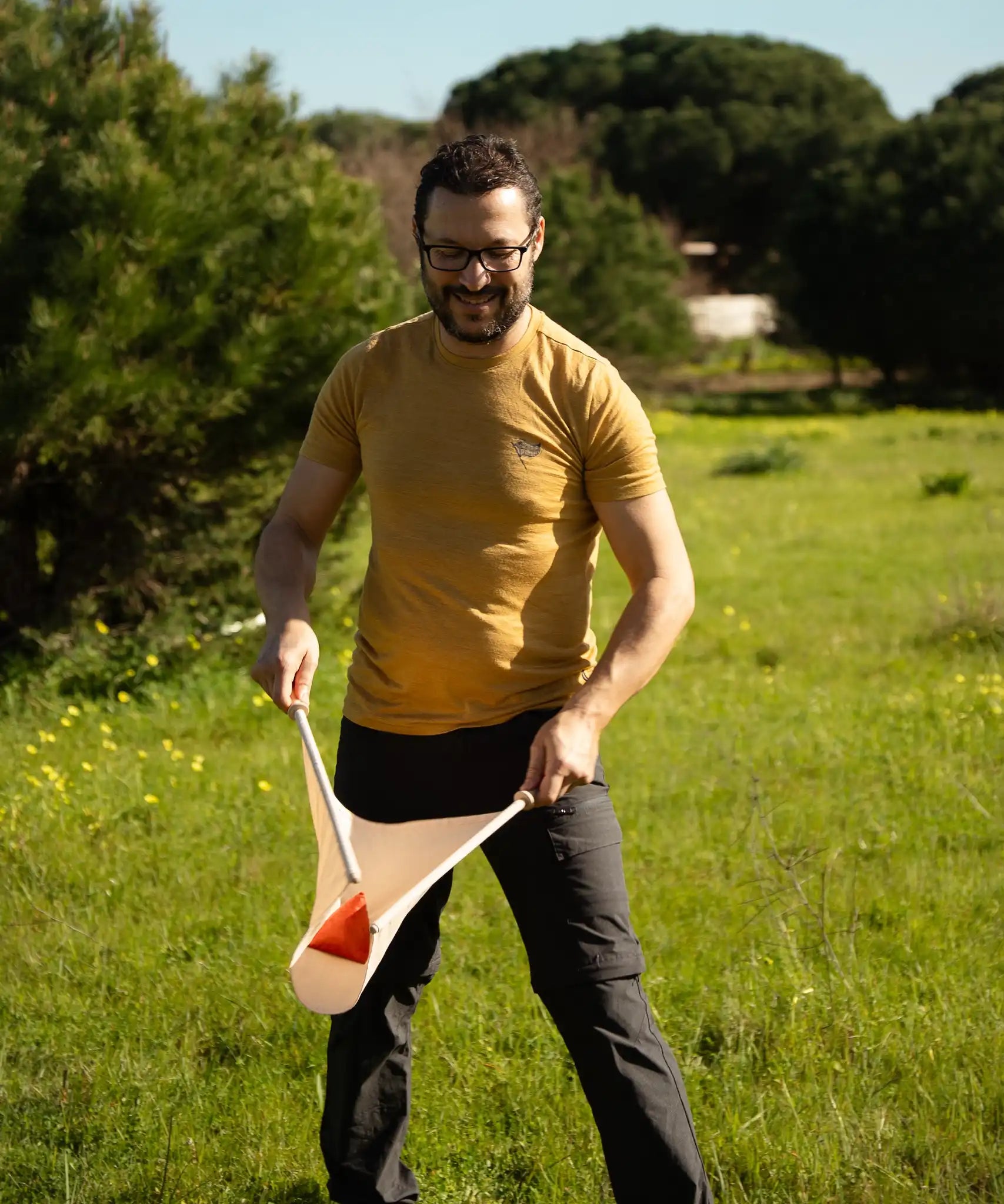 An adult playing the Flup throwing game outdoors, holding one of the fabric slings with the soft throwing bag balanced on it. 