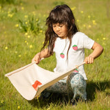 Child playing with the Flup throwing game outdoors, kneeling down holding one of the fabric slings with the throwing bag resting on it. 