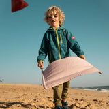 Child playing with the Flup throwing game on the beach, holding the fabric sling with the throwing bag in the air. 