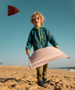 Child playing with the Flup throwing game on the beach, holding the fabric sling with the throwing bag in the air. 