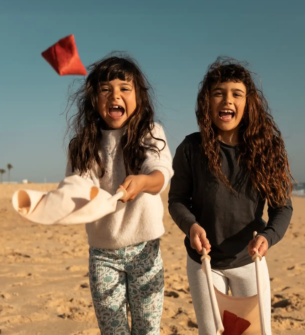 Children playing with the Flup throwing game on the beach. Each child is holding one of the fabric slings. 