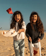 Children playing with the Flup throwing game on the beach. Each child is holding one of the fabric slings. 