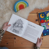 For The Children Of The World children's book by Louise deForest showing the Steiner Waldorf story pages shown open in an adult's hands in the Babipur playroom. Grimm's wooden Babi Gwawr rainbow and sparkling orient set placed on the floor.