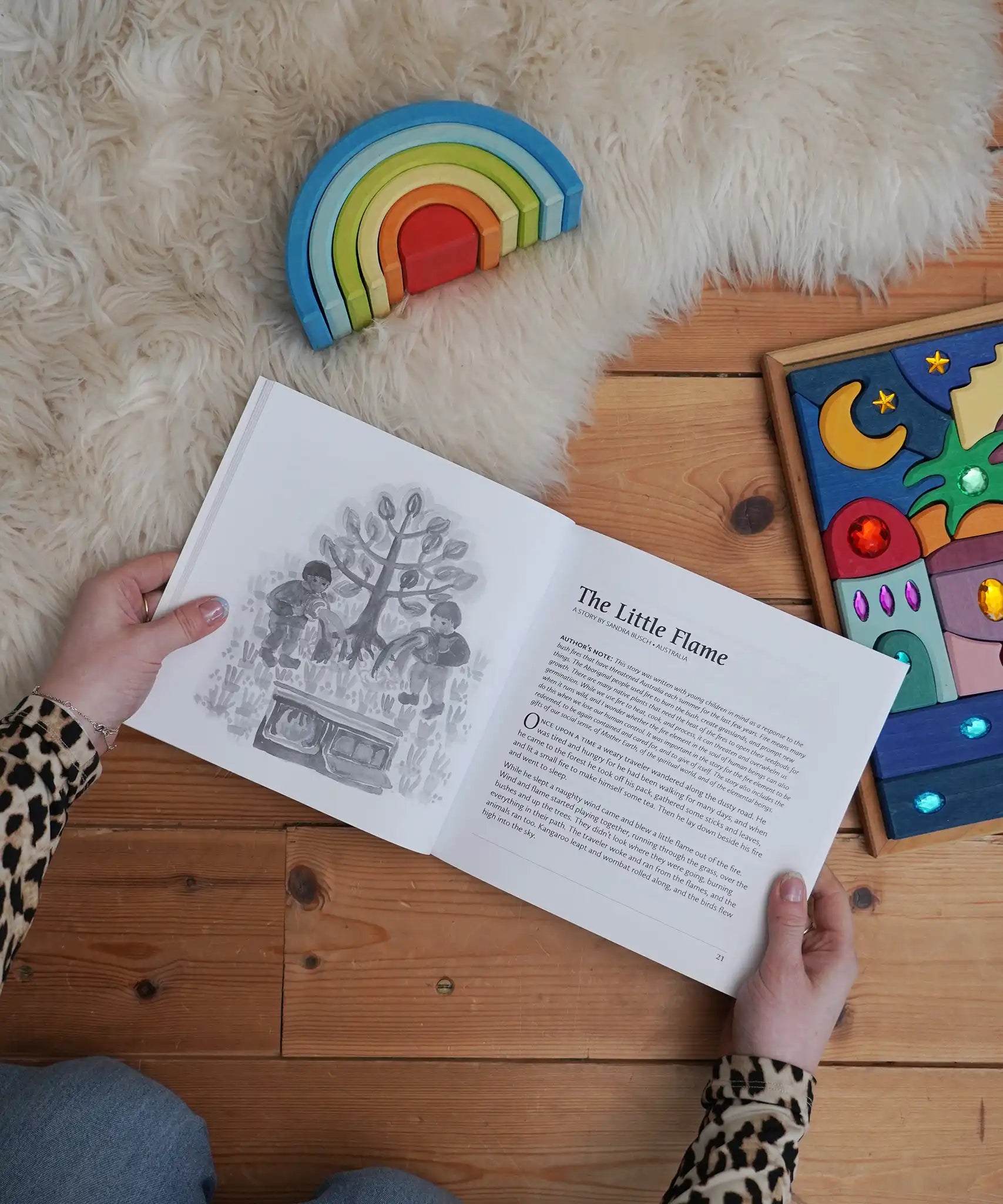 For The Children Of The World children's book by Louise deForest showing the Steiner Waldorf story pages shown open in an adult's hands in the Babipur playroom. Grimm's wooden Babi Gwawr rainbow and sparkling orient set placed on the floor.