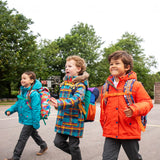 Children walking in a playground all wearing Frugi winter coats. One is wearing the penhale parker, one wearing the fire orange 3-in-one rambler coat and one wearing the boat blue 3-in-one rambler coat.